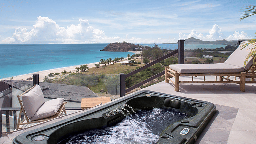 An outdoor terrace with a hot tub and lounge chairs, providing a stunning elevated view of the ocean and coastline.