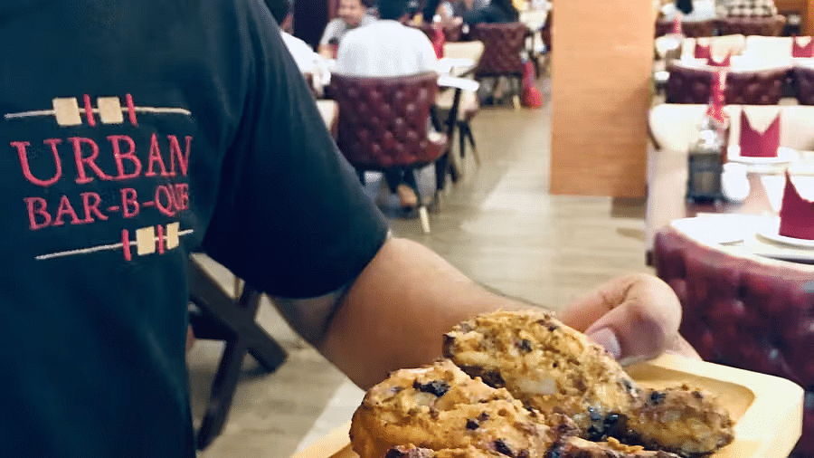 A person wearing a black t-shirt with URBAN BAR-B-QUE partially visible, holding a plate of food in a restaurant setting.
