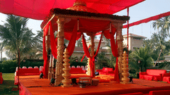 A ceremonial pavilion with decorative draping and pillars set up outdoors with palm trees in the background.