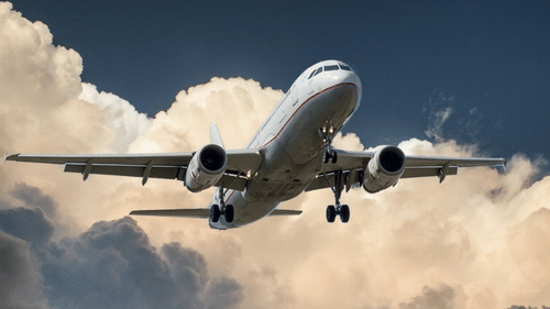 An overview of an aeroplane flying in the sky with large white clouds in the background.