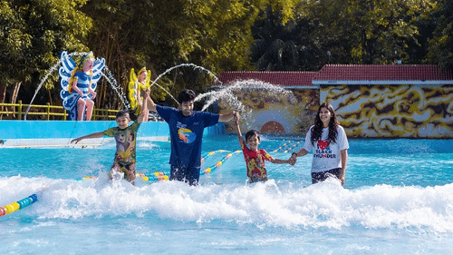 Kids enjoying water games with dolphin fountain at Black Thunder Water Theme Park, surrounded by lush greenery.