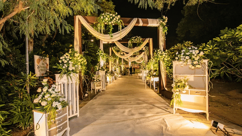 A beautifully decorated wedding entrance walkway adorned with floral arrangements, draped fabrics, ambient lighting, and elegant event décor | Clarks Amer, Jaipur