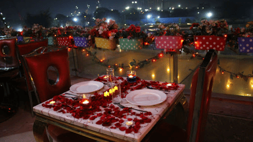 a well-decorated table with rose petals spread over dinner plates  - polo floatel kolkata