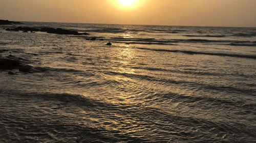 A sunset view over the sea with waves approaching the shore.