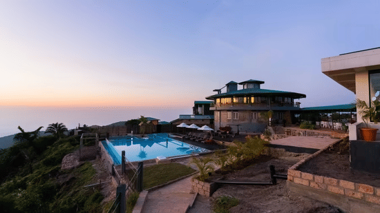 Exterior view of Polo Resort Cherrapunji at dusk showing the multi-storey resort building, outdoor swimming pool and surrounding hillside terraces.