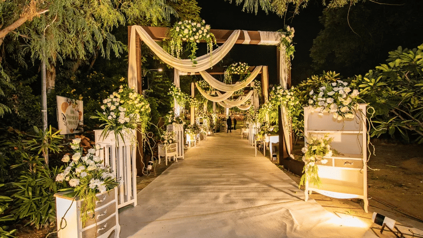 A beautifully decorated wedding entrance walkway adorned with floral arrangements, draped fabrics, ambient lighting, and elegant event décor | Clarks Amer, Jaipur