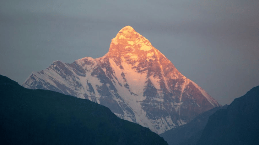The summit of a tall icy mountain, shown between two other mountains