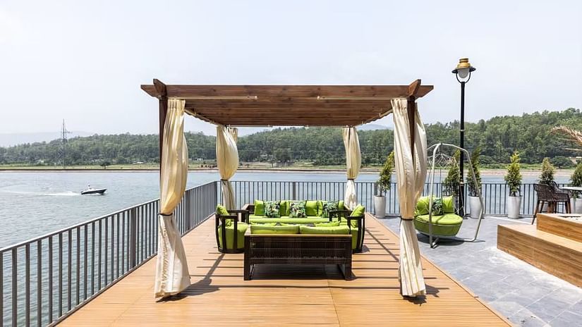 A wooden gazebo with a seating area overlooking a lake, with boats visible in the distance.