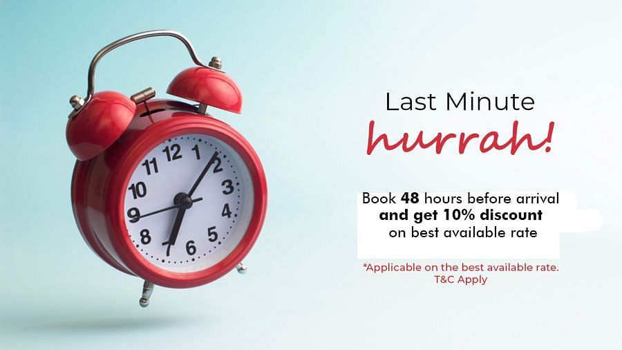 A red vintage alarm clock with two bells is set against a soft blue background. The text reads: Last Minute hurrah! Book 48 hours before arrival and get 10% discount on best available rate. *Applicable on the best available rate. T&C Apply.