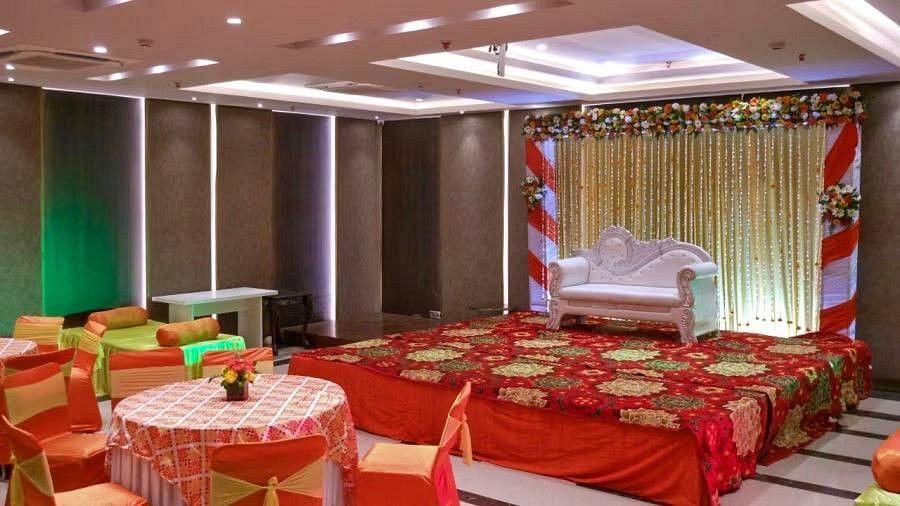 A stage is decorated with flowers in red theme and a white sofa is kept there, in front of which several decorated small circular tables are kept.
