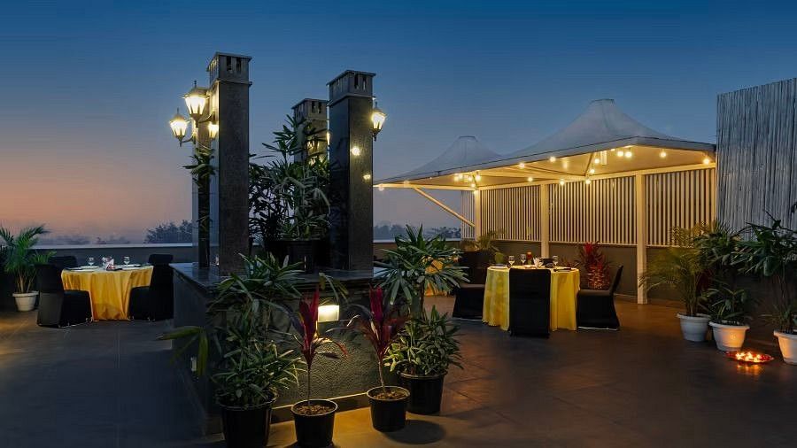 Cosy rooftop ambience featuring well-lit dining spaces, vibrant plants, and a picturesque twilight view at Hotel Saket 27.