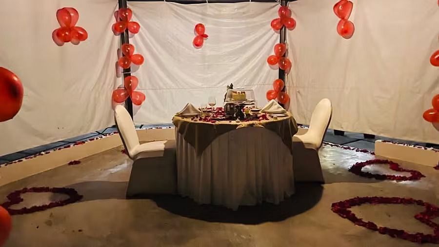 A setup with a table for two, flanked by chairs, under a draped backdrop decorated with balloons. 