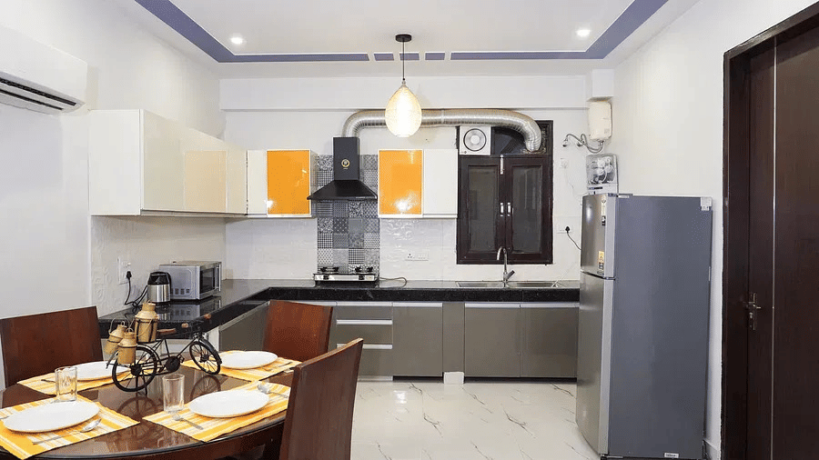 Fully equipped modular kitchen and dining space at Lime Tree 1BHK Serviced Apartment Near Medanta Hospital Gurgaon featuring cabinets cooking hob refrigerator and self catering facilities