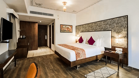 A well-lit hotel room with a plush bed, a desk, and a TV. - Bamboo Saa Resort & Spa, Udaipur