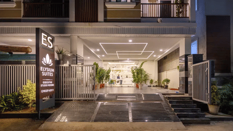 The lit entrance of the Elysium Hotel at night, showing a ramp, steps, and a large sign beside a glass-walled lobby at ELYSIUM Hotels.
