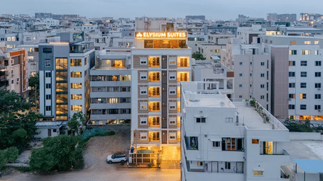 High-angle shot of a multi-storey hotel building at dusk, illuminated against a dense urban skyline under an overcast grey sky at ELYSIUM Hotels.