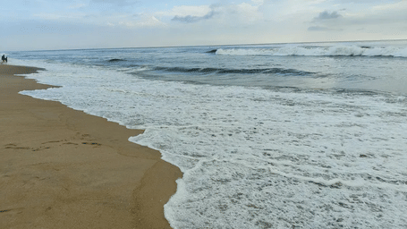 Foamy white sea waves crashing onto a sandy beach coastline under a soft daylight overcast sky.