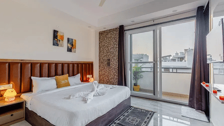 Bedroom of Lime Tree Hotels & Service Apartment Private Limited featuring a wooden headboard, white bedding, and a balcony with glass doors.