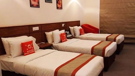 View of three beds arranged in Max Club Room with photo frames mounted on the wall in the background - Max Hotel Prayagraj.