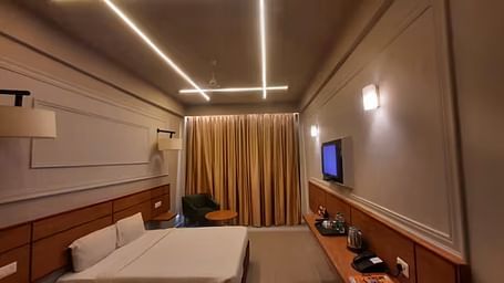 View of a modern hotel room with ambient lighting, a comfortable bed, and a wall-mounted TV - Max Hotel Prayagraj.