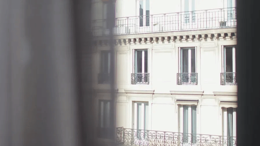 A partial view through a window reveals a multi storey hotel building facade featuring symmetry, regular windows, and classic balconies.