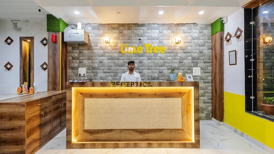 A hotel reception area with a wooden counter, yellow accents, and a stone-textured wall - Lime Tree Hotels & Banquet, Vrindavan