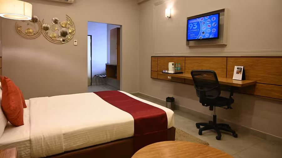 View of a neat hotel room featuring a bed, a wall-mounted TV, a work desk, and warm lighting - Max Hotel Prayagraj.