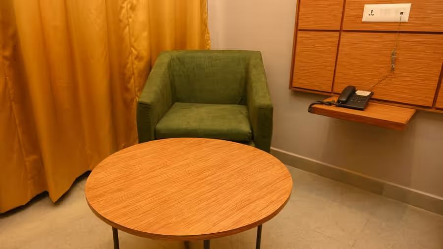  A cosy seating space with a round wooden table and a comfortable green armchair - Max Hotel Prayagraj.