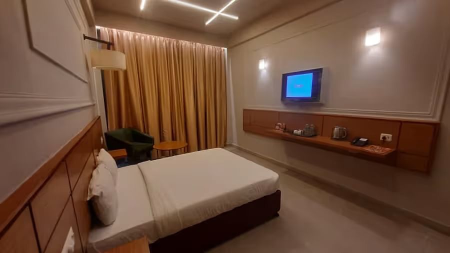 View of a well-lit and spacious hotel room with a bed, tv, cosy bedding and a modern interior in premium room - Max Hotel Prayagraj.
