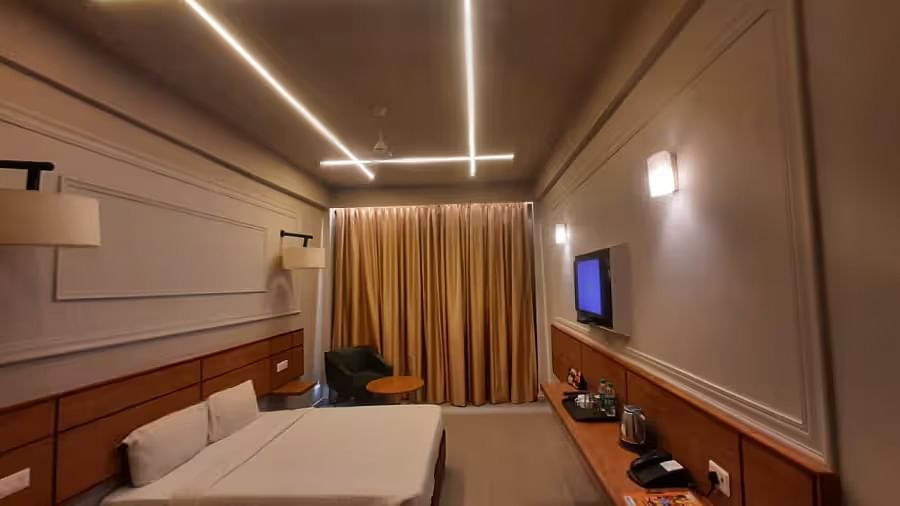 View of a modern hotel room with ambient lighting, a comfortable bed, and a wall-mounted TV - Max Hotel Prayagraj.