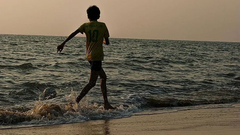 A boy runs along the shoreline, splashing through gentle waves with the sea and horizon in the background.