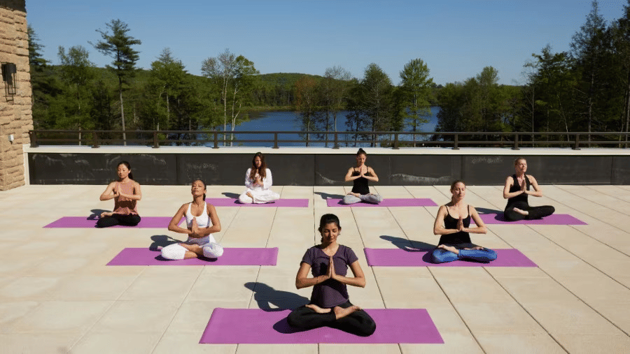 A group of 7 people on yoga mat meditating on a rooftop with a lush background at YO1 Longevity and Health Resorts, Catskills