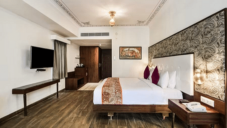 A well-lit hotel room with a plush bed, pillows, a desk, and a TV.- Bamboo Saa Resort & Spa, Udaipur