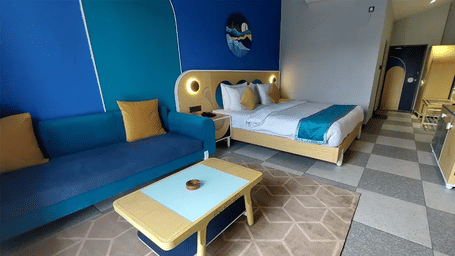A large room featuring a bed, a sofa with a table in front of it over a carpet at Hotel Sonar Bangla, Mayapur.