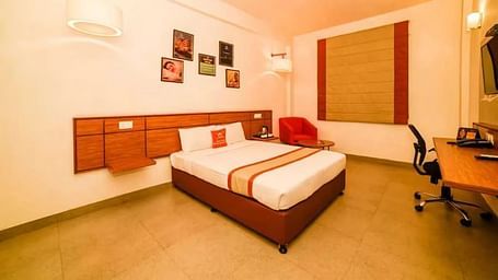 Well-lit hotel room with a double bed, wooden furniture, and wall art - Max Hotel Prayagraj