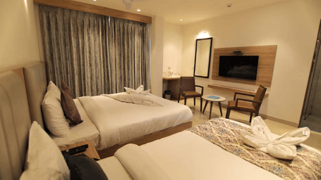 Room at Hotel Mumbai House Express, Udaipur, with beds, bedspreads, pillows, a large windows with curtains, and a television.