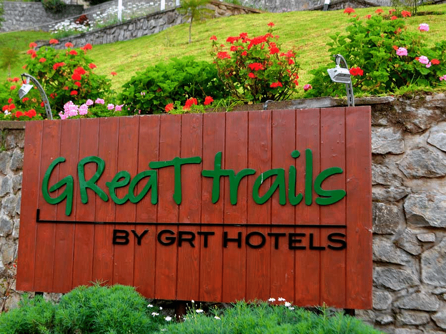 Signboard reading 'Great Trails by GRT Hotels' surrounded by vibrant flowers.
