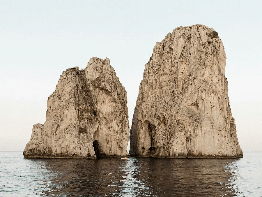 wo large rock formations rising out of the water near a coastline.