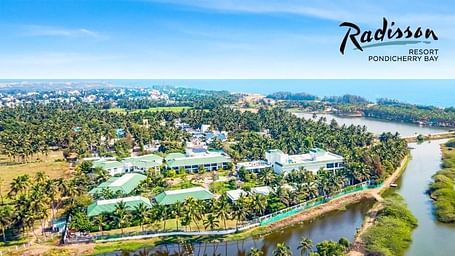 Aerial view of Radisson Pondicherry Bay with lush greenery, a lagoon, and the sea in the background.