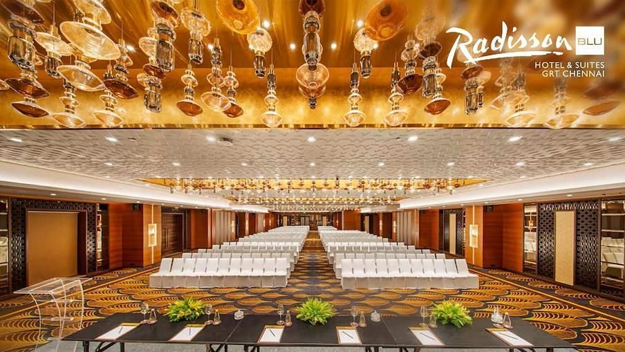 Elegant conference hall at Radisson Blu Hotel & Suites GRT Chennai with golden chandeliers and seating setup.
