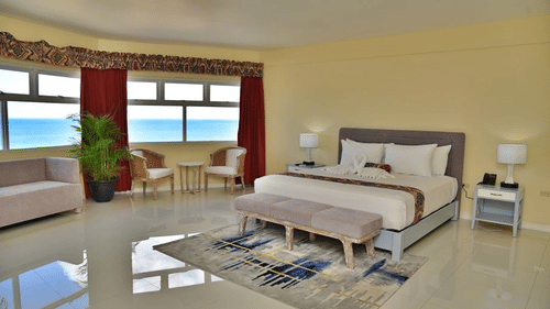 Deluxe Ocean View Room featuring a plush bed with a sitting space including a couple chairs and a sofa by the window with the view of the seaHotel Grand A View