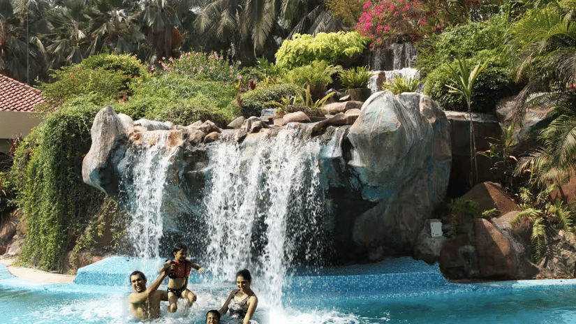 A Waterfall flowing over rocks into a blue pool surrounded by tropical plants and palm trees.