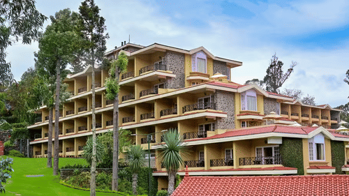 The multi-storey facade of the Clarton Hotel in Kodaikanal amidst the greenery, under a partly clouded blue sky.