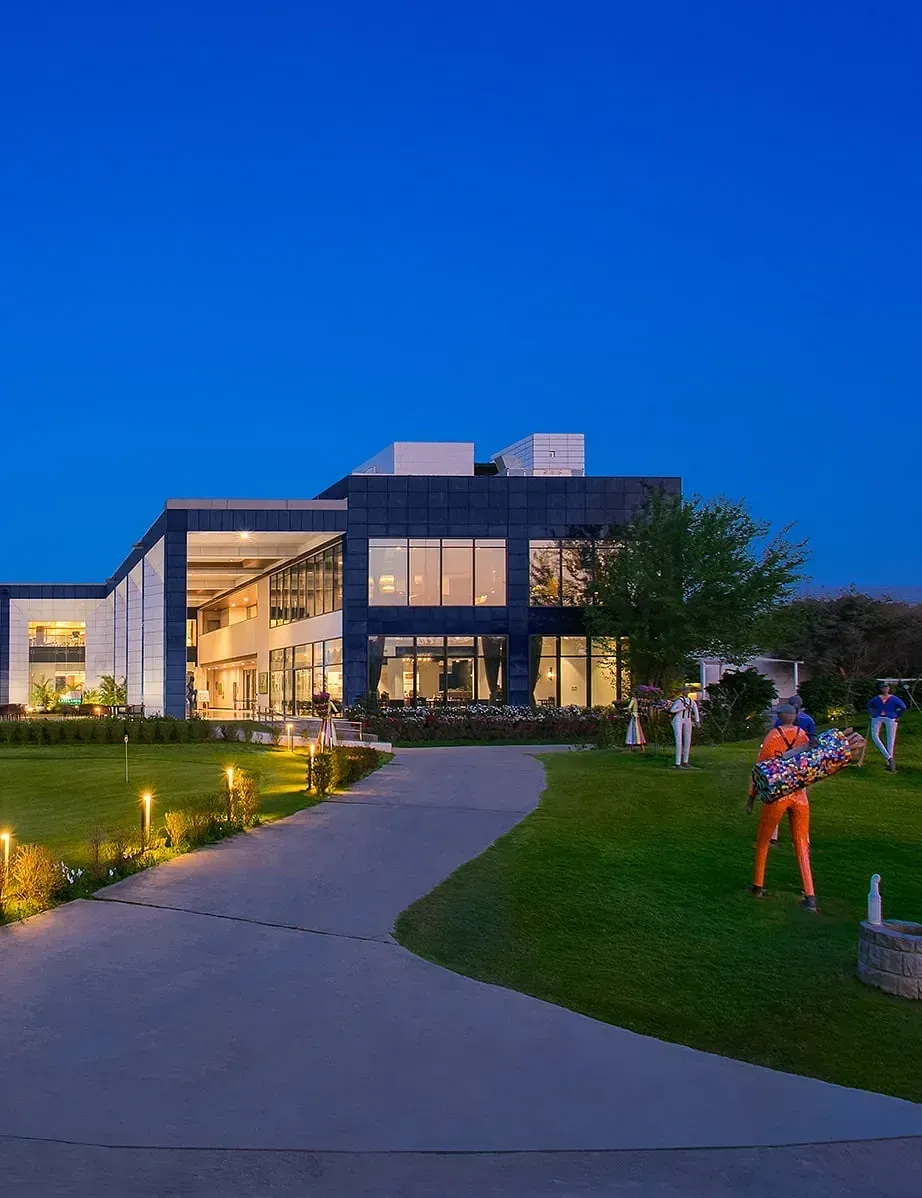 A building lit up at night with a large lawn in front and people walking along a curved pathway at Karma Chalets.