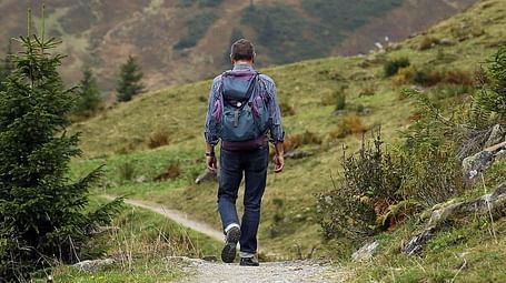 Image of a person from the back hiking down a mountain path with trees in the background.