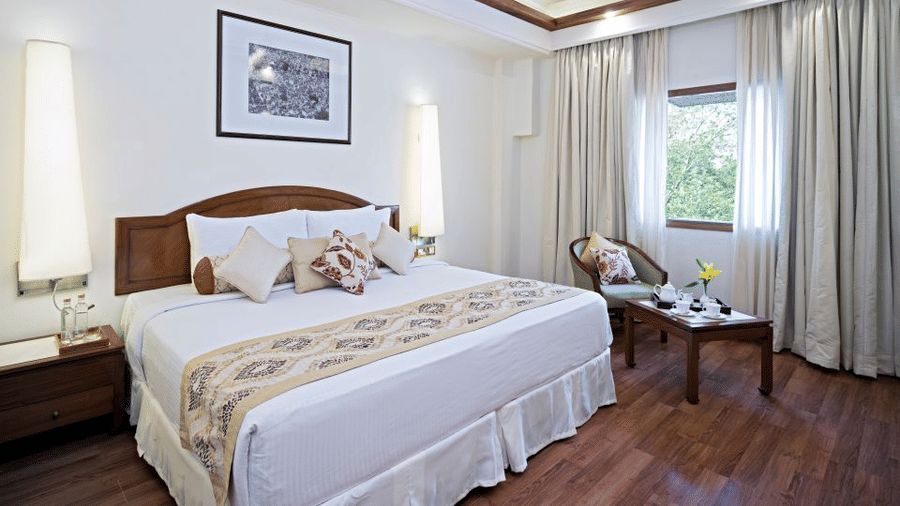 The classy interiors with a calming white aesthetic of Superior Rooms at Clarks Amer, Jaipur featuring a plush bed and a sitting space next to the window