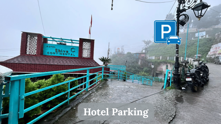 Hotel Shiva Continental parking area with car parking space on a misty hillside road.