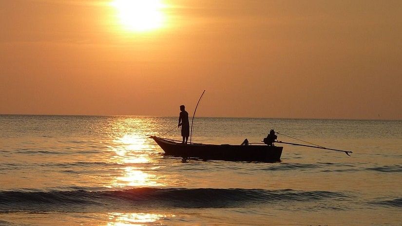 Silhouette of two people on a small boat at sea during sunset.