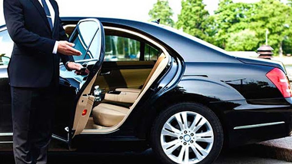 A chauffeur in a suit and tie opens the back door of a black luxury car.