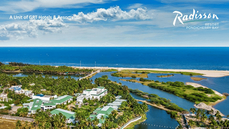 A scenic aerial view of Radisson Resort Pondicherry Bay showing lush greenery, winding waterways and the coastline promoting the Winter Waves meeting offer.